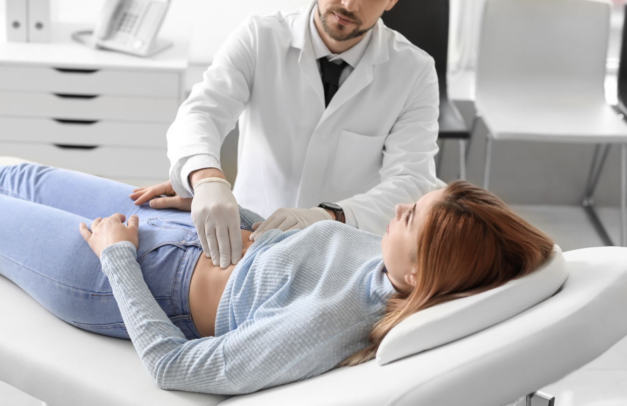Clinician performing abdominal exam on female patient, assessing gut health in the context of hormonal or autoimmune symptoms.