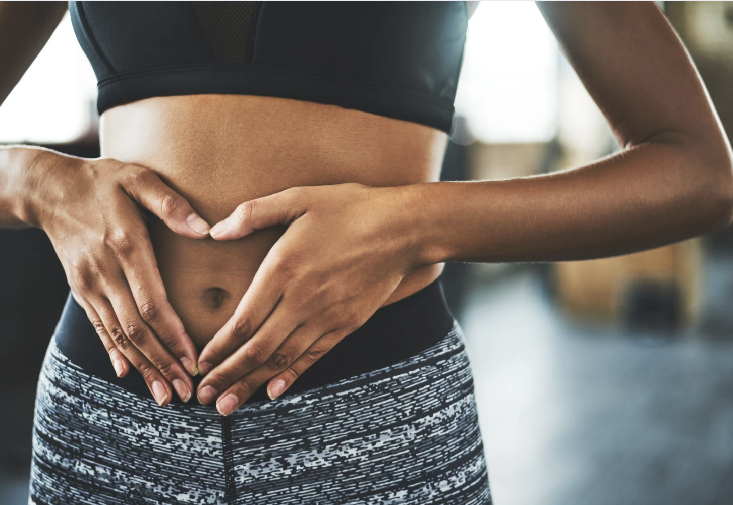 Woman in athletic wear forming a heart shape with her hands over her stomach, symbolizing gut health and well-being.